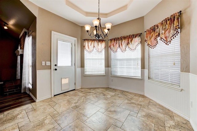 unfurnished dining area featuring a wainscoted wall, a tray ceiling, and a chandelier