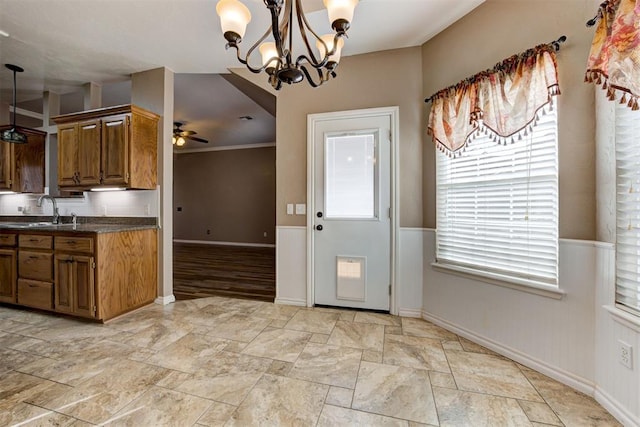 kitchen featuring ceiling fan with notable chandelier, dark countertops, a sink, and brown cabinets