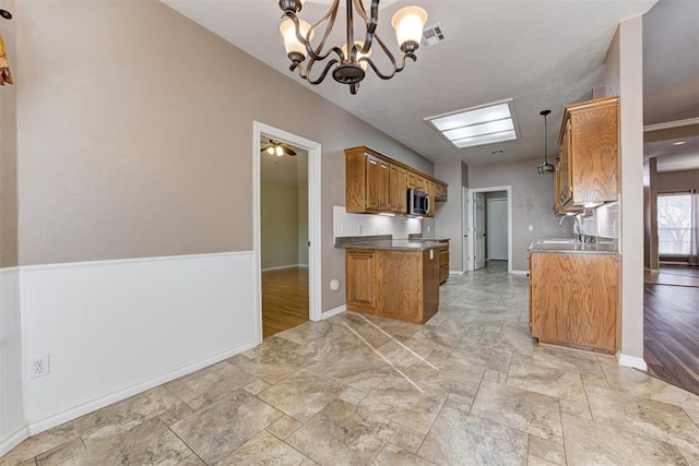 kitchen with a sink, visible vents, brown cabinetry, stainless steel microwave, and decorative light fixtures