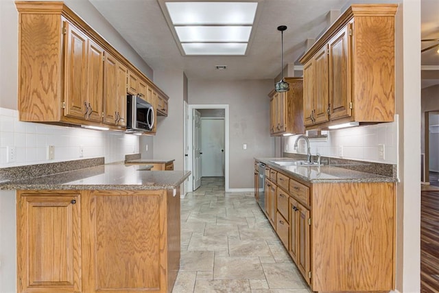 kitchen with stainless steel appliances, a peninsula, a sink, baseboards, and stone finish flooring