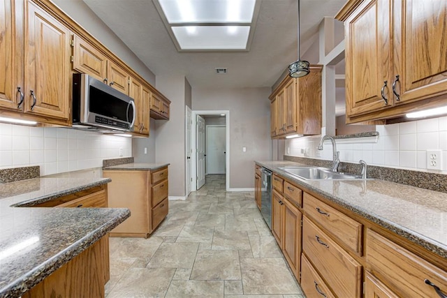 kitchen with baseboards, dark stone counters, appliances with stainless steel finishes, stone finish flooring, and a sink