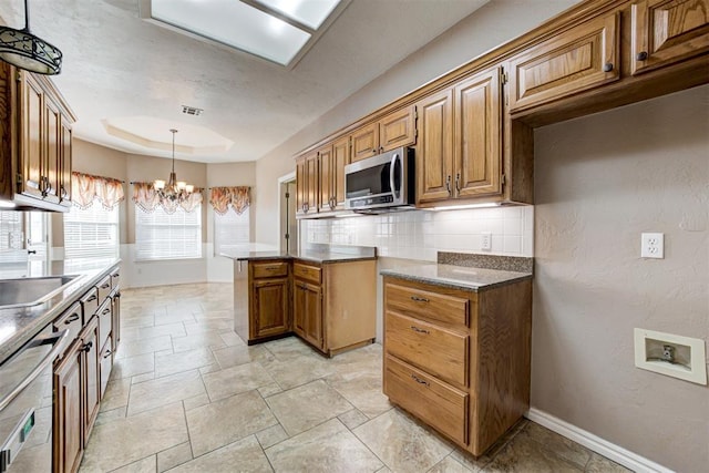 kitchen with brown cabinets, stainless steel microwave, a raised ceiling, and a notable chandelier