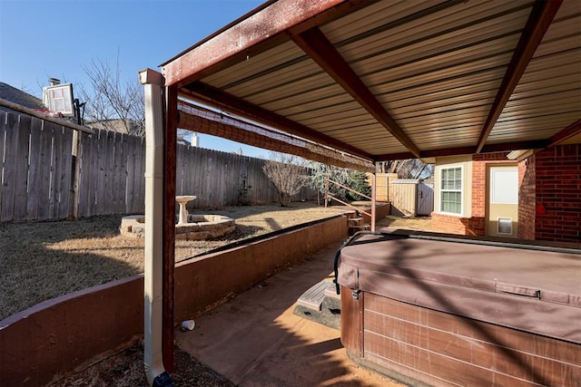 view of patio with a storage shed, an outbuilding, fence private yard, and a hot tub