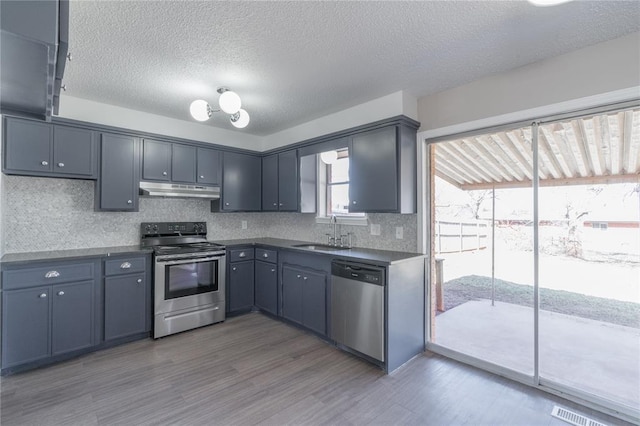 kitchen with decorative backsplash, dark countertops, a sink, under cabinet range hood, and stainless steel appliances