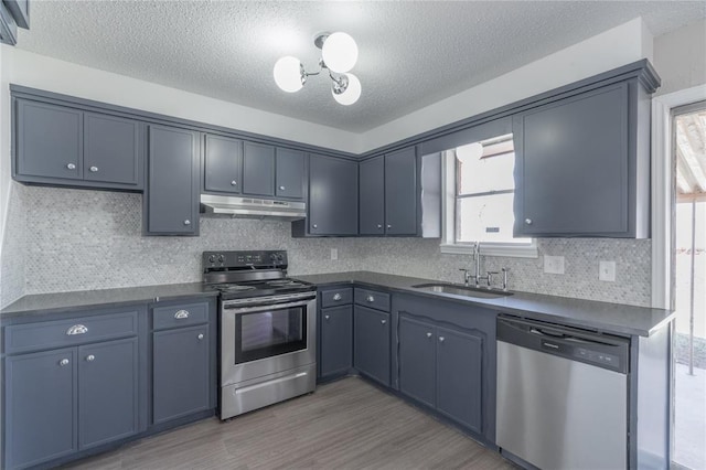 kitchen with dark countertops, a sink, a textured ceiling, stainless steel appliances, and under cabinet range hood