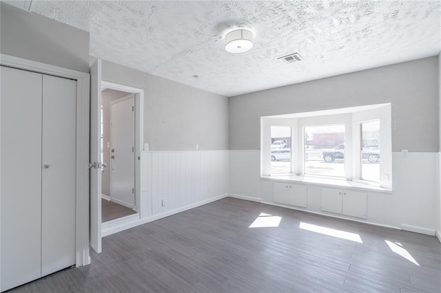 unfurnished bedroom with visible vents, a textured ceiling, wood finished floors, and a wainscoted wall