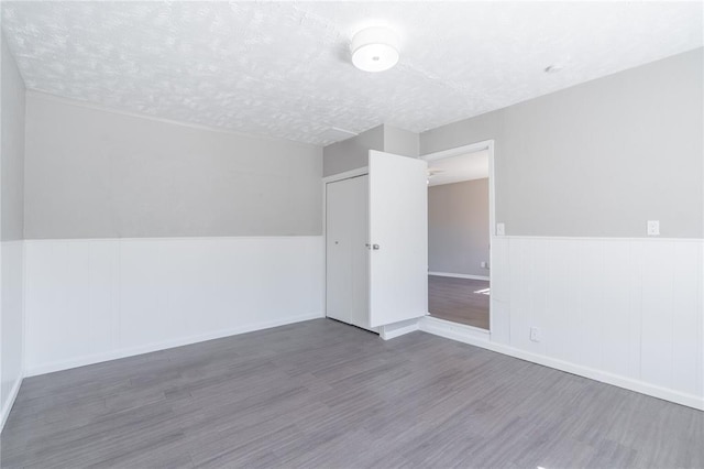 unfurnished room featuring a textured ceiling, wainscoting, and wood finished floors