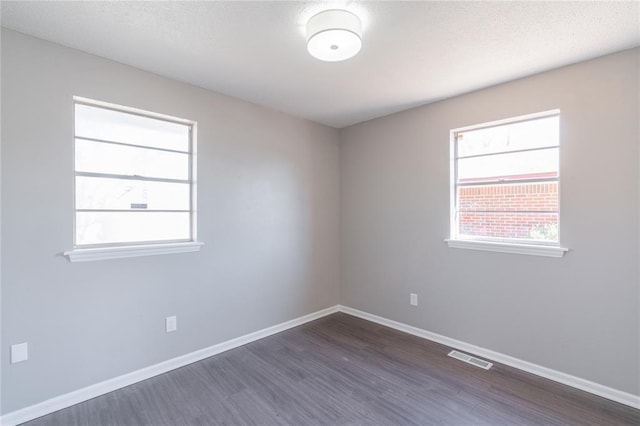 spare room featuring baseboards, dark wood finished floors, a textured ceiling, and visible vents