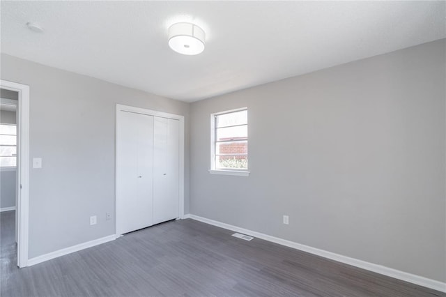 unfurnished bedroom featuring baseboards, a closet, dark wood-style flooring, and visible vents