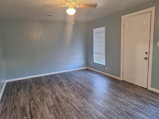 spare room featuring dark wood-style floors, visible vents, baseboards, and a ceiling fan