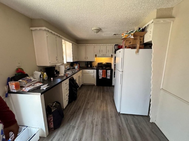 kitchen with dark countertops, black stove, wood finished floors, and freestanding refrigerator