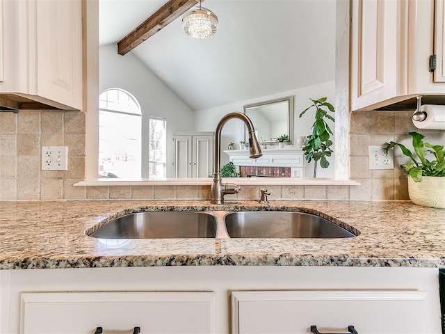 kitchen featuring lofted ceiling with beams, light stone countertops, tasteful backsplash, and a sink