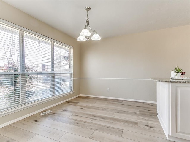 empty room with light wood-style floors, visible vents, baseboards, and a notable chandelier