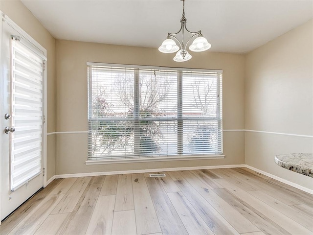 unfurnished dining area with a healthy amount of sunlight, visible vents, a chandelier, and wood finished floors