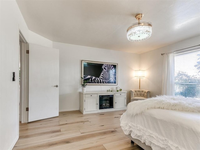 bedroom with light wood-style flooring, baseboards, and a glass covered fireplace