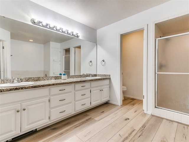 bathroom featuring toilet, a stall shower, a sink, and wood finished floors