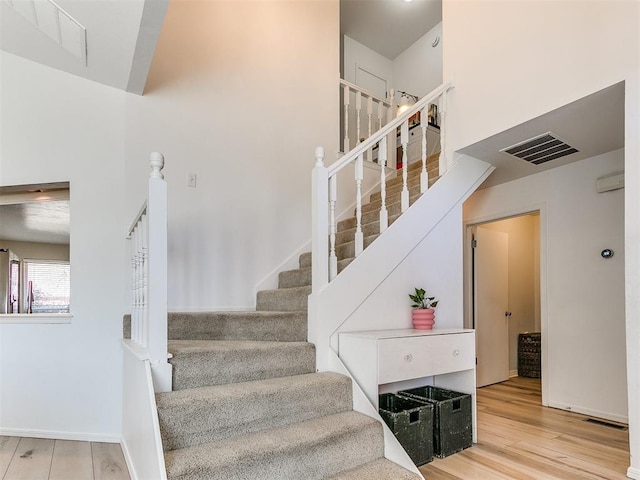 staircase with a high ceiling, visible vents, and wood finished floors