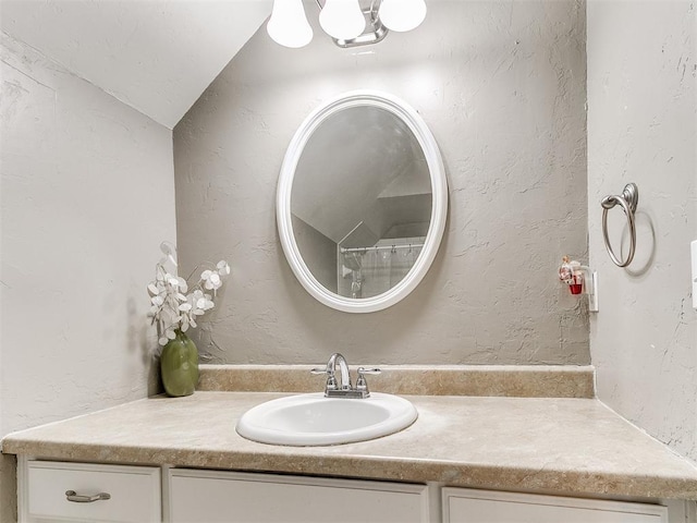 bathroom featuring lofted ceiling, a textured wall, and vanity