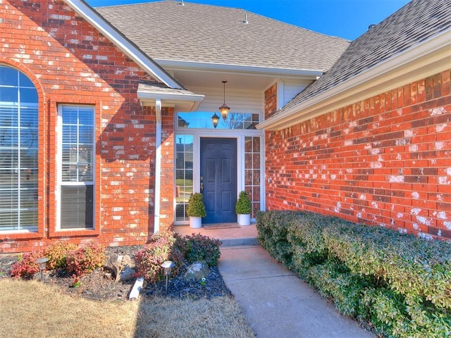 entrance to property featuring brick siding and roof with shingles