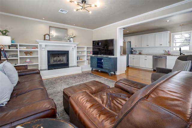 living area with a fireplace with raised hearth, a chandelier, visible vents, light wood-style floors, and ornamental molding