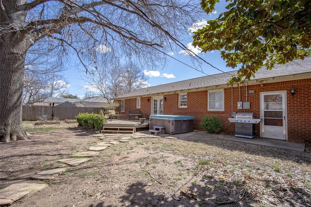 rear view of house featuring brick siding, fence, a wooden deck, and a hot tub