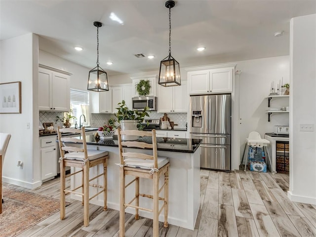 kitchen with white cabinets, decorative backsplash, dark countertops, light wood-style flooring, and stainless steel appliances