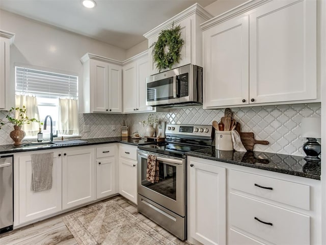 kitchen featuring stainless steel appliances, decorative backsplash, white cabinets, a sink, and dark stone countertops