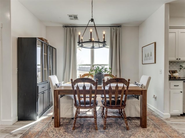 dining area with a chandelier, light wood-type flooring, visible vents, and baseboards