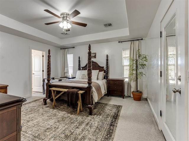 bedroom with light colored carpet, a raised ceiling, visible vents, and baseboards