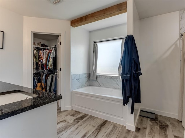 full bathroom featuring baseboards, wood finished floors, a walk in closet, vanity, and a bath