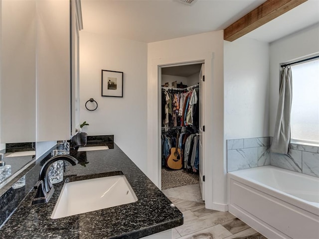 full bathroom with a garden tub, beam ceiling, a sink, and a walk in closet