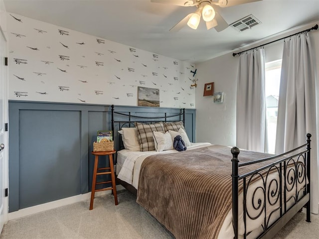 bedroom with light carpet, wallpapered walls, visible vents, a ceiling fan, and wainscoting