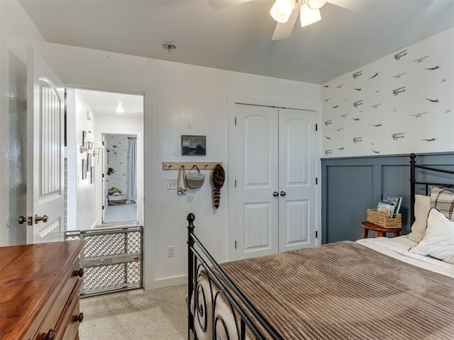 bedroom featuring light carpet, wallpapered walls, a ceiling fan, a wainscoted wall, and a closet