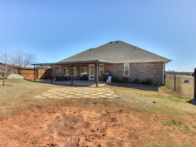 back of property with a shingled roof, a lawn, a patio, a fenced backyard, and brick siding