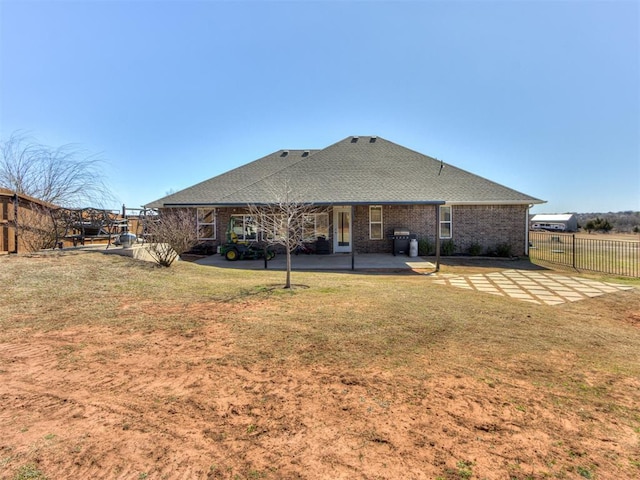 rear view of property with roof with shingles, a yard, brick siding, a patio, and fence