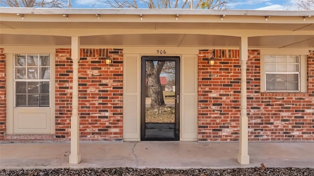 view of exterior entry with a porch and brick siding