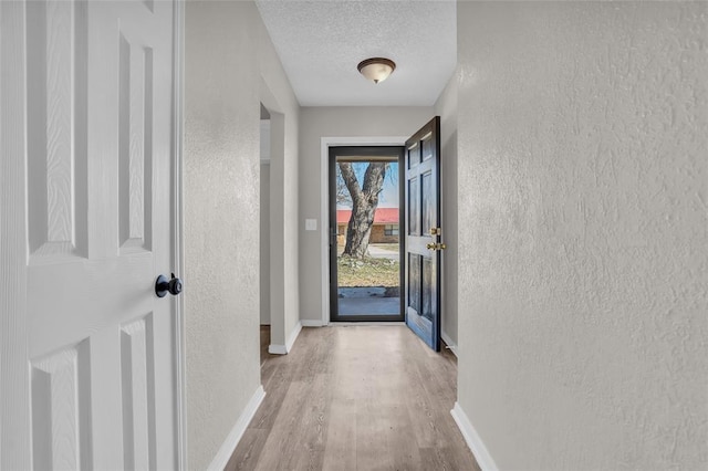 doorway to outside featuring a textured wall, a textured ceiling, baseboards, and wood finished floors