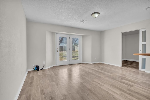 empty room with baseboards, a textured ceiling, visible vents, and light wood-style floors