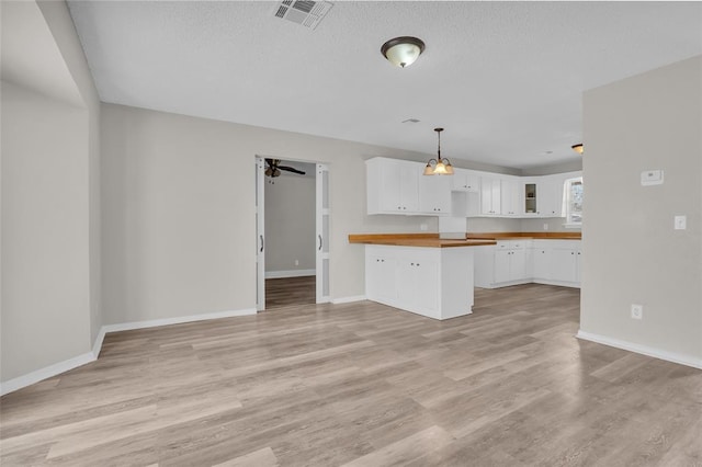 kitchen featuring light wood-style flooring, a peninsula, visible vents, white cabinetry, and glass insert cabinets