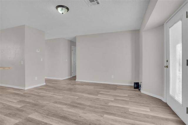 spare room featuring light wood-style floors, visible vents, a textured ceiling, and baseboards