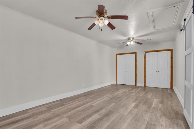 unfurnished bedroom with baseboards, two closets, attic access, and light wood-style floors