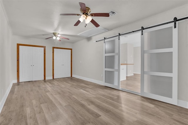 unfurnished bedroom with light wood-type flooring, two closets, baseboards, and a barn door