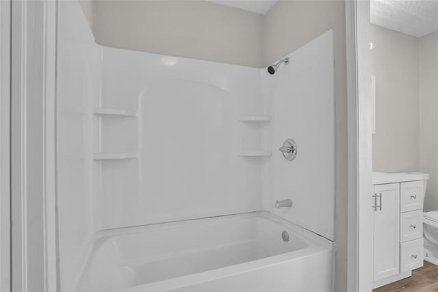 full bathroom featuring toilet, washtub / shower combination, a textured ceiling, and wood finished floors