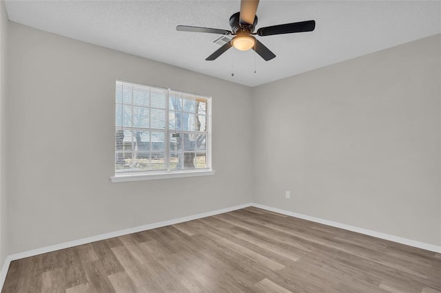 empty room with ceiling fan, a textured ceiling, baseboards, and wood finished floors