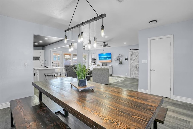 dining area featuring a barn door, baseboards, ceiling fan, and wood finished floors