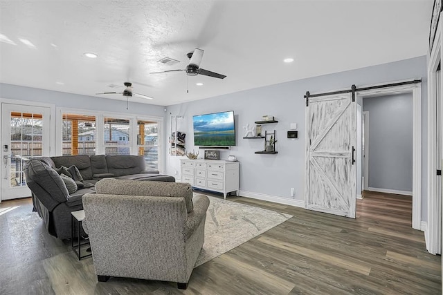 living room featuring a barn door, a ceiling fan, visible vents, baseboards, and dark wood finished floors