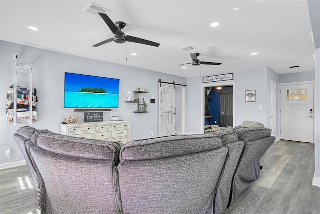 living room with ceiling fan, a barn door, light wood-type flooring, and visible vents