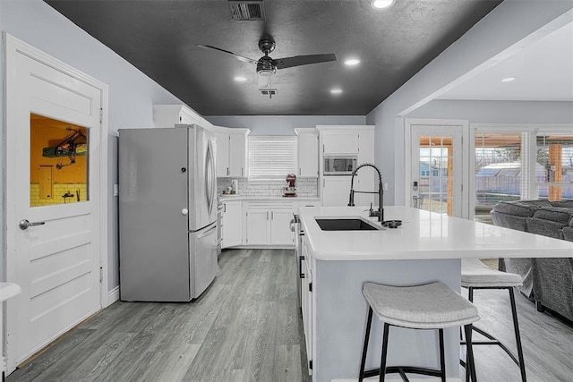 kitchen with visible vents, backsplash, appliances with stainless steel finishes, a sink, and light wood-type flooring