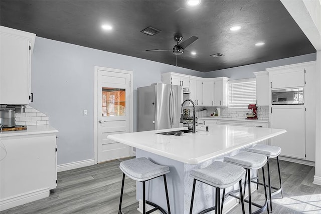 kitchen with appliances with stainless steel finishes, visible vents, light wood-style floors, and a sink