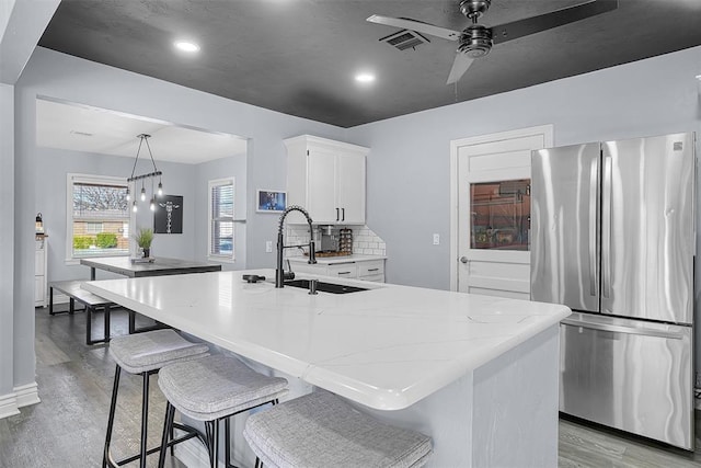 kitchen with light stone counters, freestanding refrigerator, a sink, and light wood finished floors